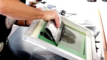 Person screen printing with a squeegee tool.