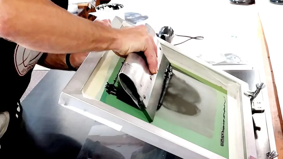 Person screen printing with a squeegee tool.