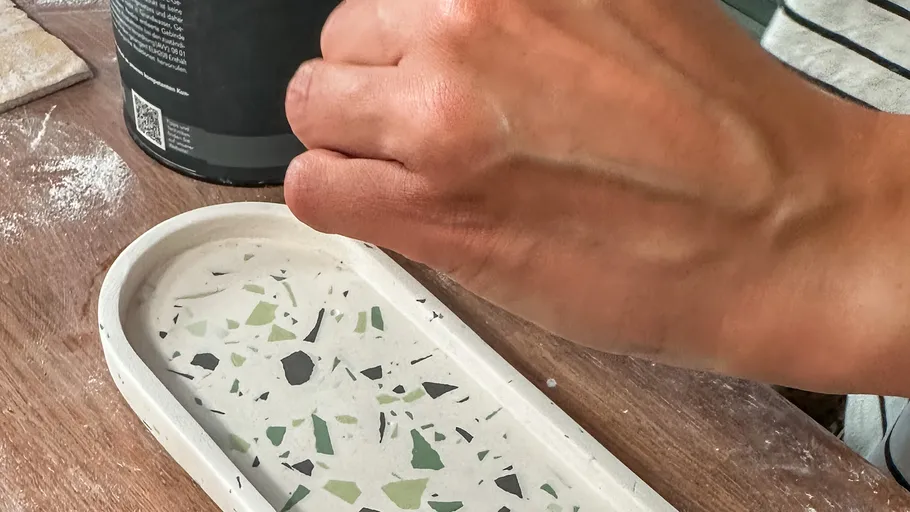 Hand fertigt ovales Terrazzo-Tablett auf Tisch.