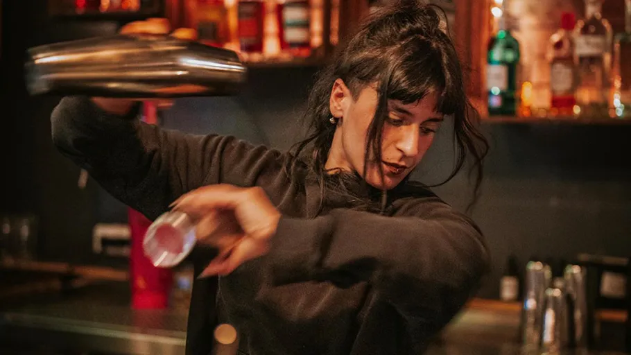 Barkeeper schüttelt Cocktail in schummriger Bar.