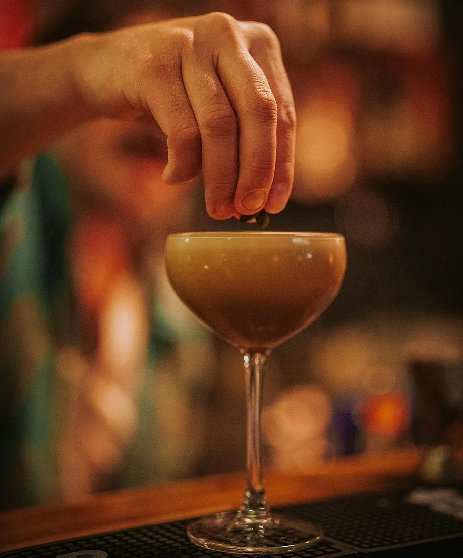 Hand garnishing a cocktail in a dim bar.