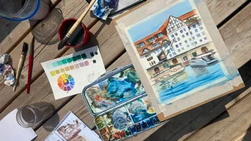 Watercolor painting supplies on wooden table.