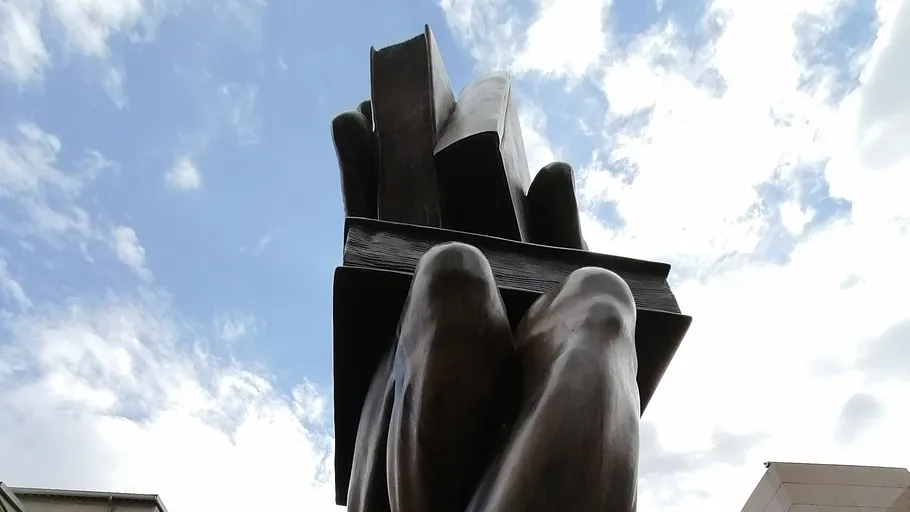 Giant hand holding books against sky.