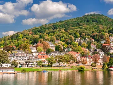 River, houses are reflected, surrounded by hills and trees.