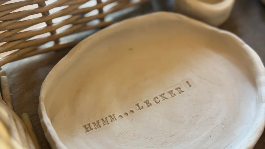 Clay plate with 'HMMM... LECKER!' text, wicker background.