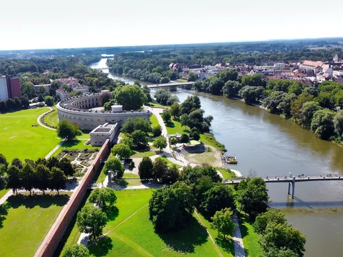 Historic fortress across a river in green parkland.