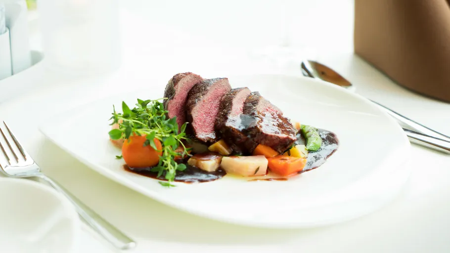 Sliced steak with vegetables on white plate.