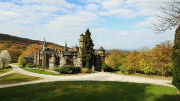 Schloss in grüner Landschaft unter blauem Himmel.