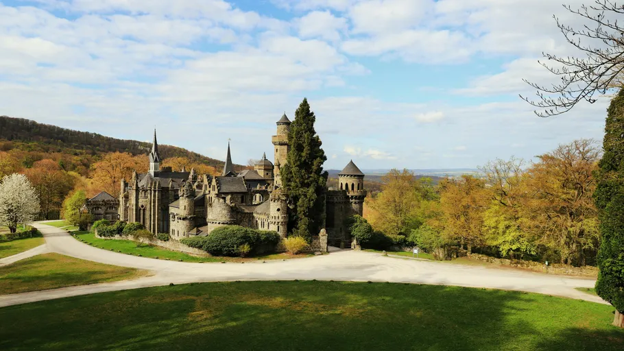 Castle in lush landscape under blue sky.