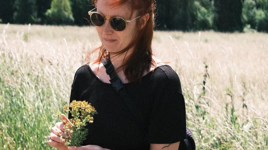 Frau mit Sonnenbrille hält Blumen auf einem Feld.