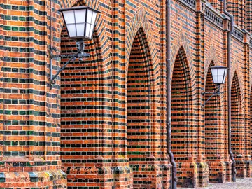 Brick wall with arches and street lamps in an urban setting.