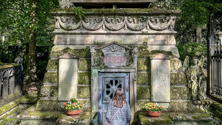 Woman observes moss-covered tomb in a cemetery.