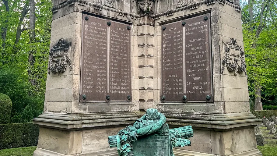 Monument with plaques and wreath in park.
