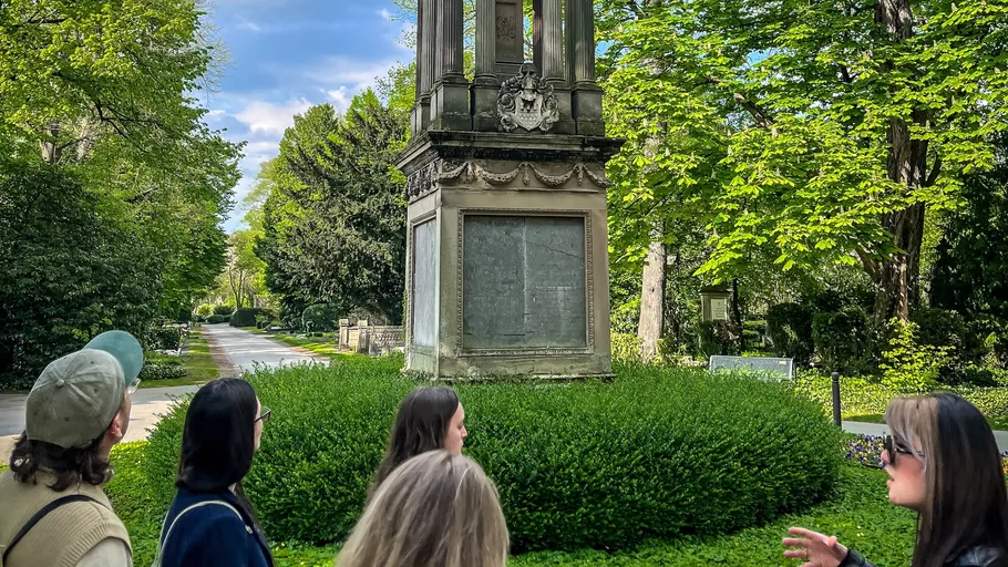 Group observing monument in lush park.