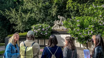 Five people observe a cemetery sculpture outdoors.