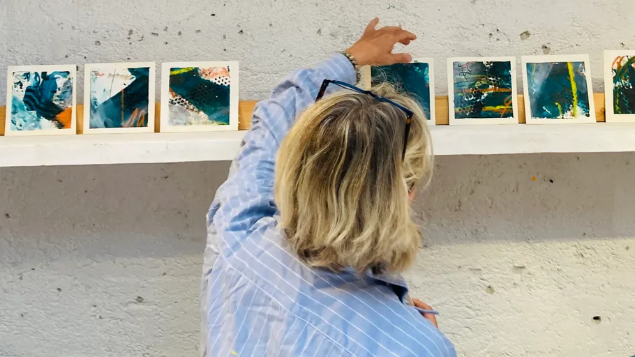 Person arranging small paintings on a wall shelf.