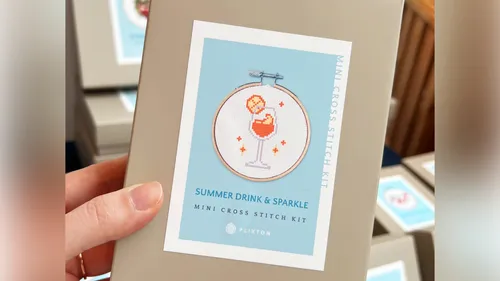 Hand holding cross stitch kit box with drink design.