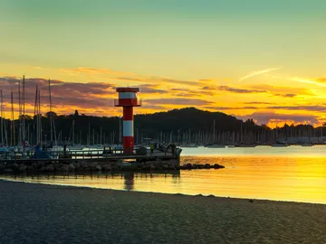 Leuchtturm steht am Ufer, während die Sonne untergeht.