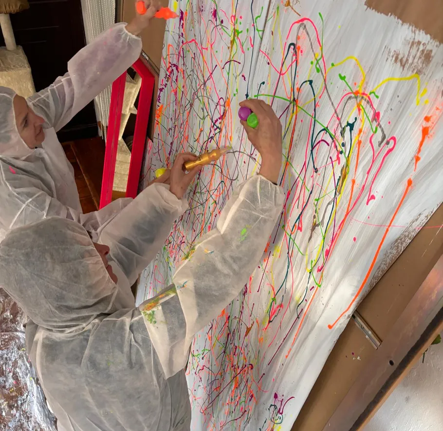 Zwei Personen in Schutzanzügen malen abstrakte Kunst.