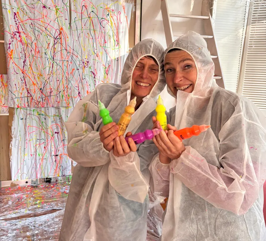 Two people in suits holding colorful paint bottles.