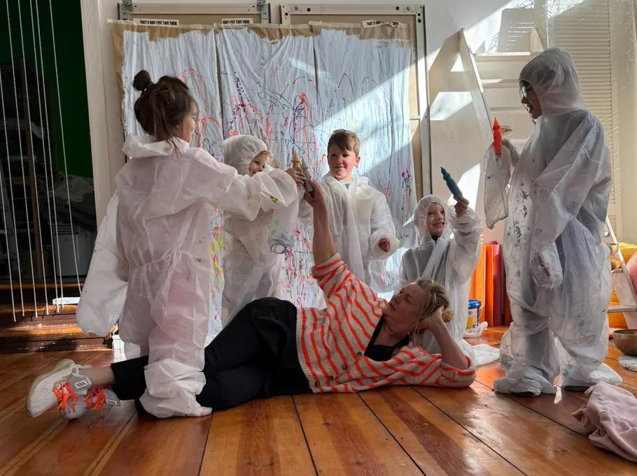 Children painting with woman on floor, indoors.