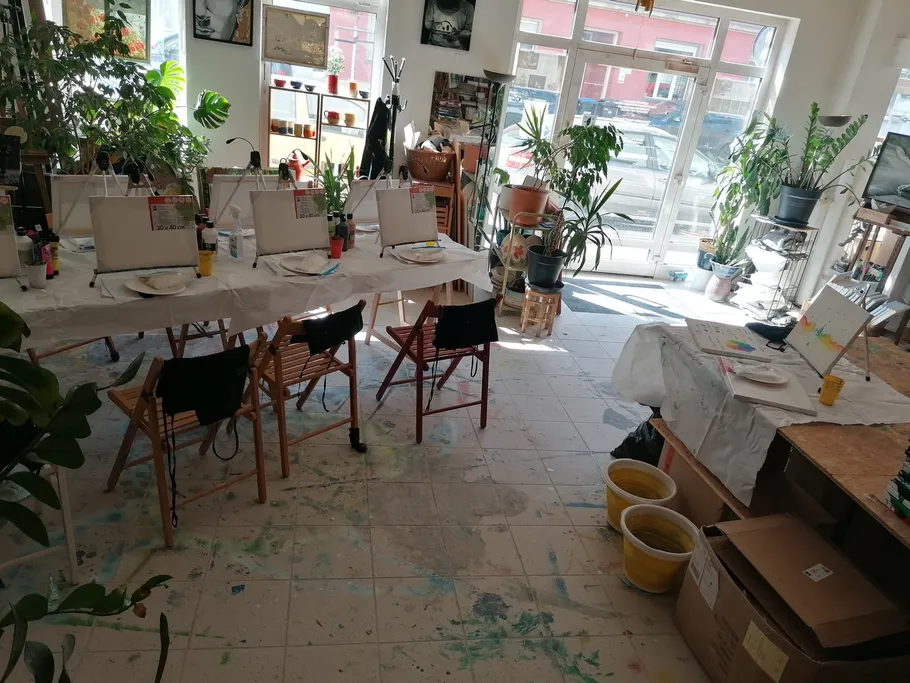 Malutensilien auf Tischen in einem hellen Atelier mit Pflanzen.