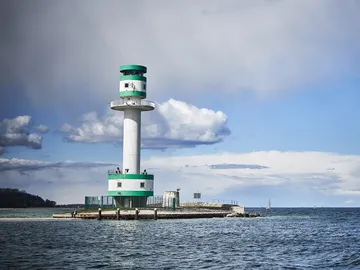 Lighthouse stands in water, surrounded by clouds and sky.
