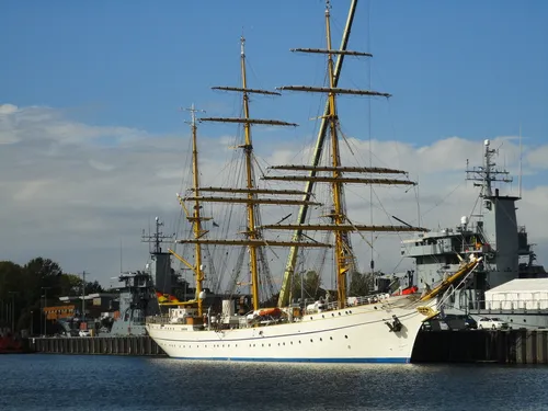 A sailing ship is moored at a harbor surrounded by other ships.