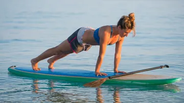 Person doing yoga plank on paddleboard in water.