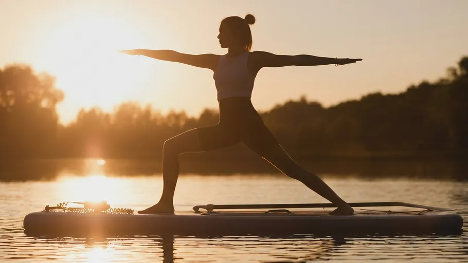 Frau macht Yoga auf Paddleboard bei Sonnenuntergang.