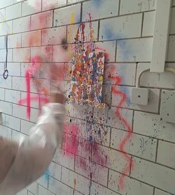 Person painting on colorful tiled wall.