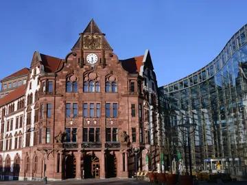 Historisches Rathaus steht neben modernem Glasgebäude, klarer Himmel.