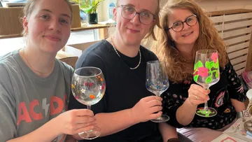 Drei Frauen halten bemalte Weingläser drinnen.