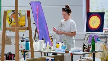 Frau malt in einem Atelier mit Staffeleien.