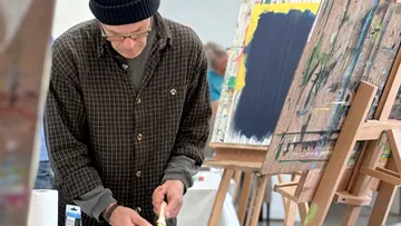 Man painting at easel in art studio.