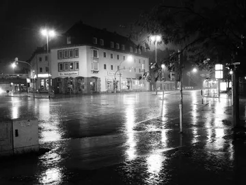 Nasse Straße mit beleuchteten Gebäuden bei Nacht.