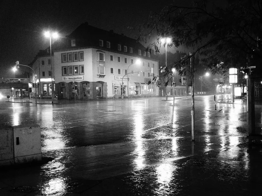 Nasse Straße mit beleuchteten Gebäuden bei Nacht.