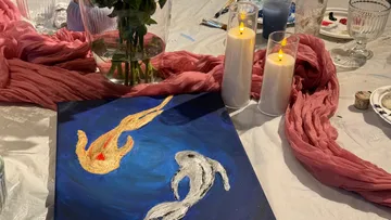 Gemälde auf Tisch mit Kerzen und Blumen.