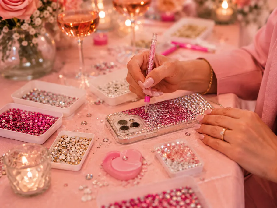 Person decorating phone case with rhinestones, pink setting.