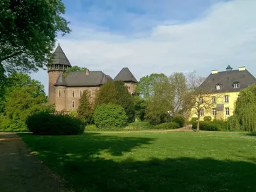 Zwei Gebäude stehen in einem grünen Park unter blauem Himmel.