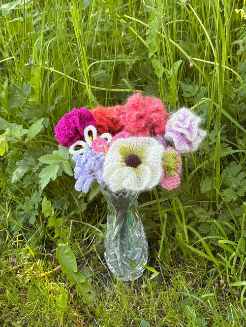 Knitted flowers in glass vase on grass.