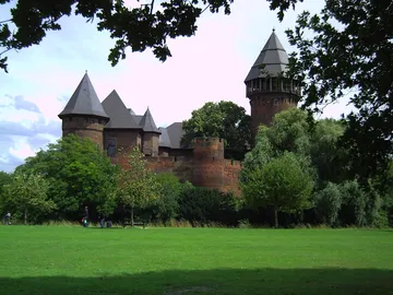 A castle is surrounded by trees and meadows.