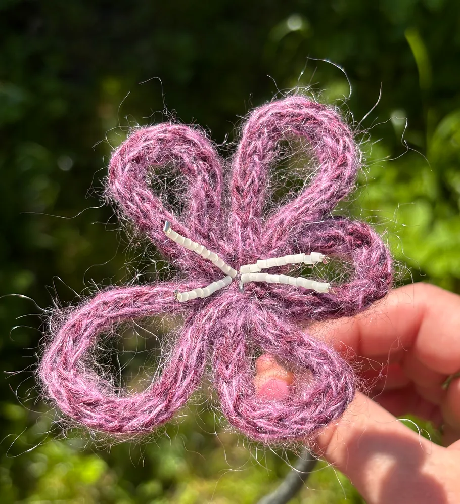 Purple yarn flower held in sunlight.
