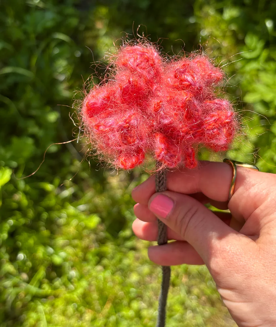 Hand holding red fuzzy flower outdoors.