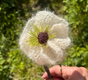 Hand holds knitted flower in garden.
