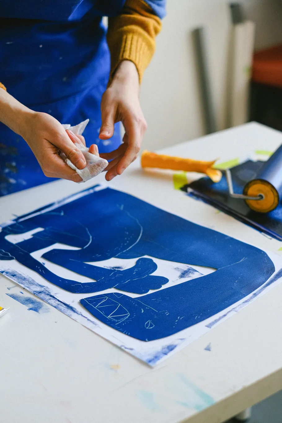 Person reinigt Kunstwerk auf Tisch mit Rolle.