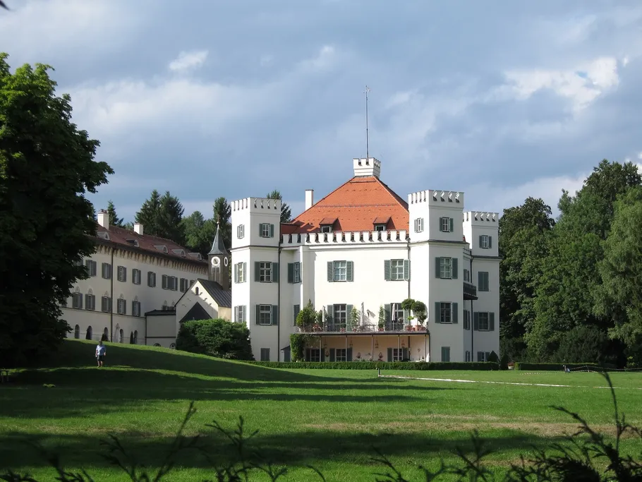 Castle stands in a meadow under a cloudy sky.