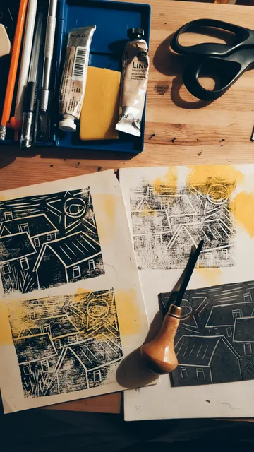 Printmaking tools and prints on a wooden table.