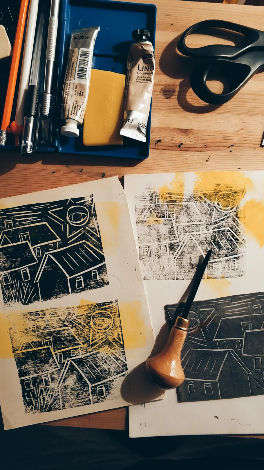 Printmaking tools and prints on a wooden table.