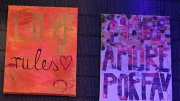Zwei bunte Leinwände mit Text an dunkler Wand.